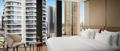 Una habitación de hotel moderna con una cama grande, una silla, una mesita y vistas a altos edificios.