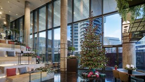 A spacious lobby with a large Christmas tree, seating areas, and a view of the cityscape through large windows.