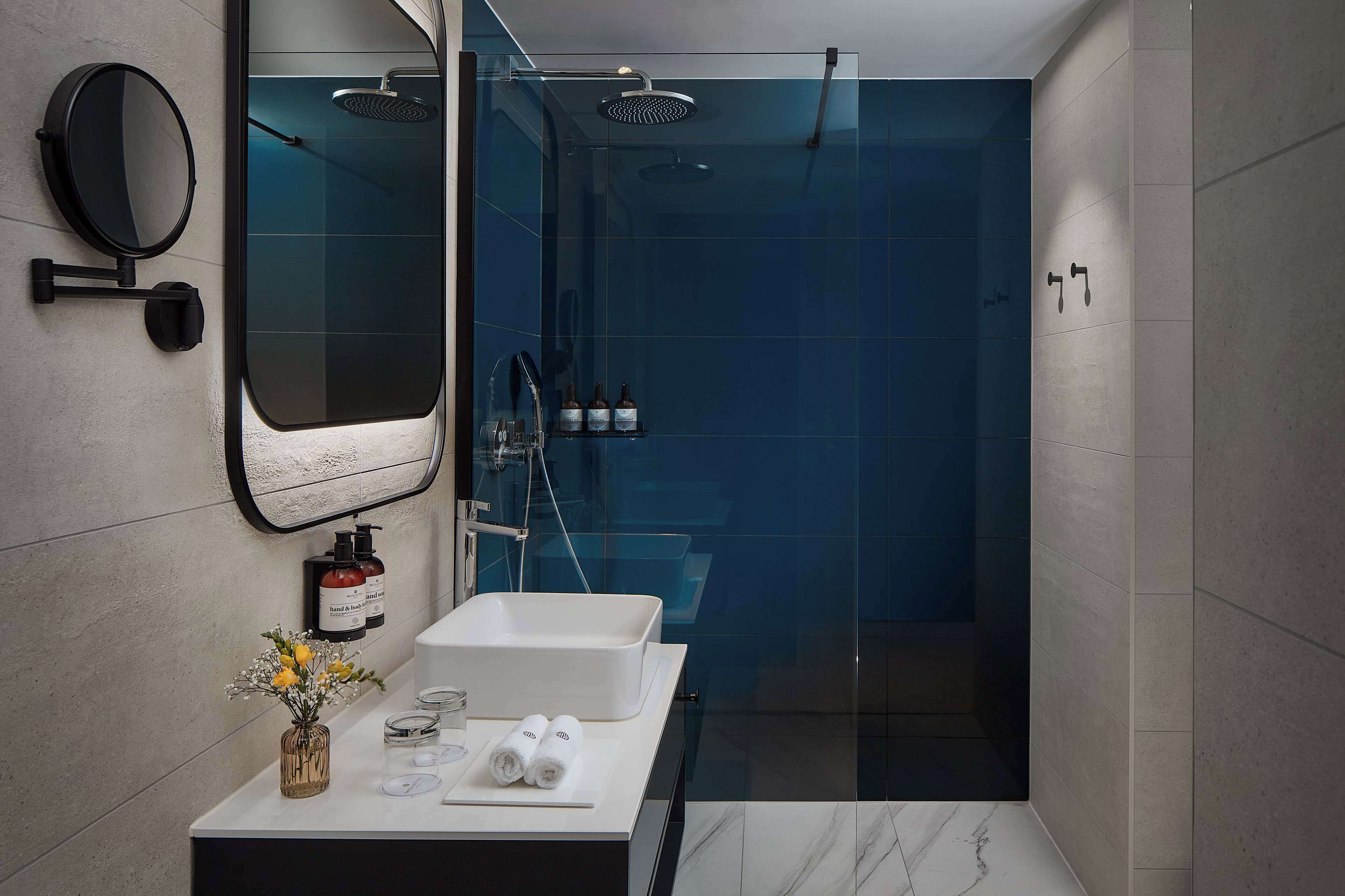 Un baño moderno con ducha de vidrio, un espejo redondo, un lavabo blanco y artículos de aseo en la encimera.
