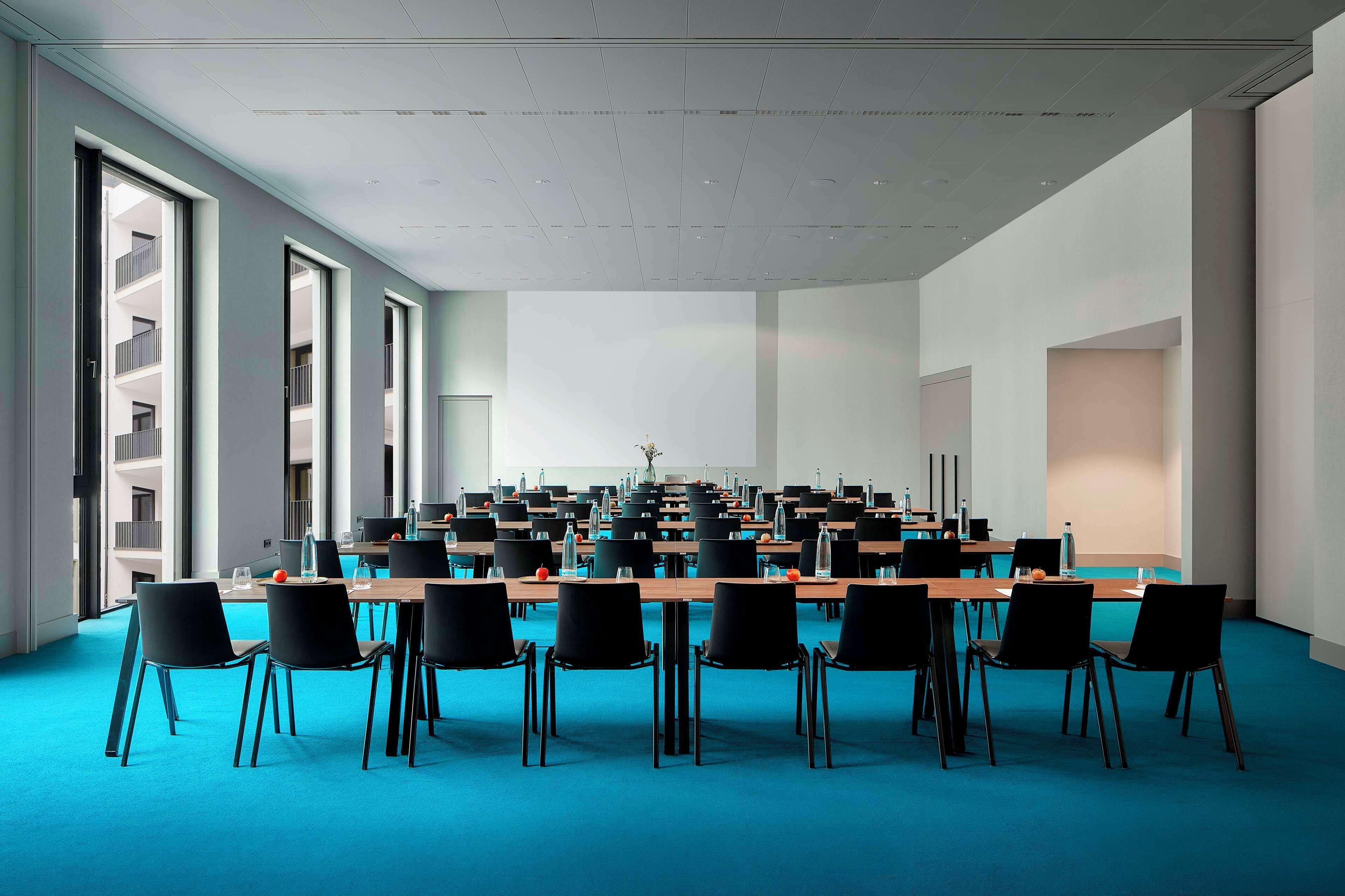 Una sala de conferencias con una larga mesa, sillas negras y una alfombra azul.
