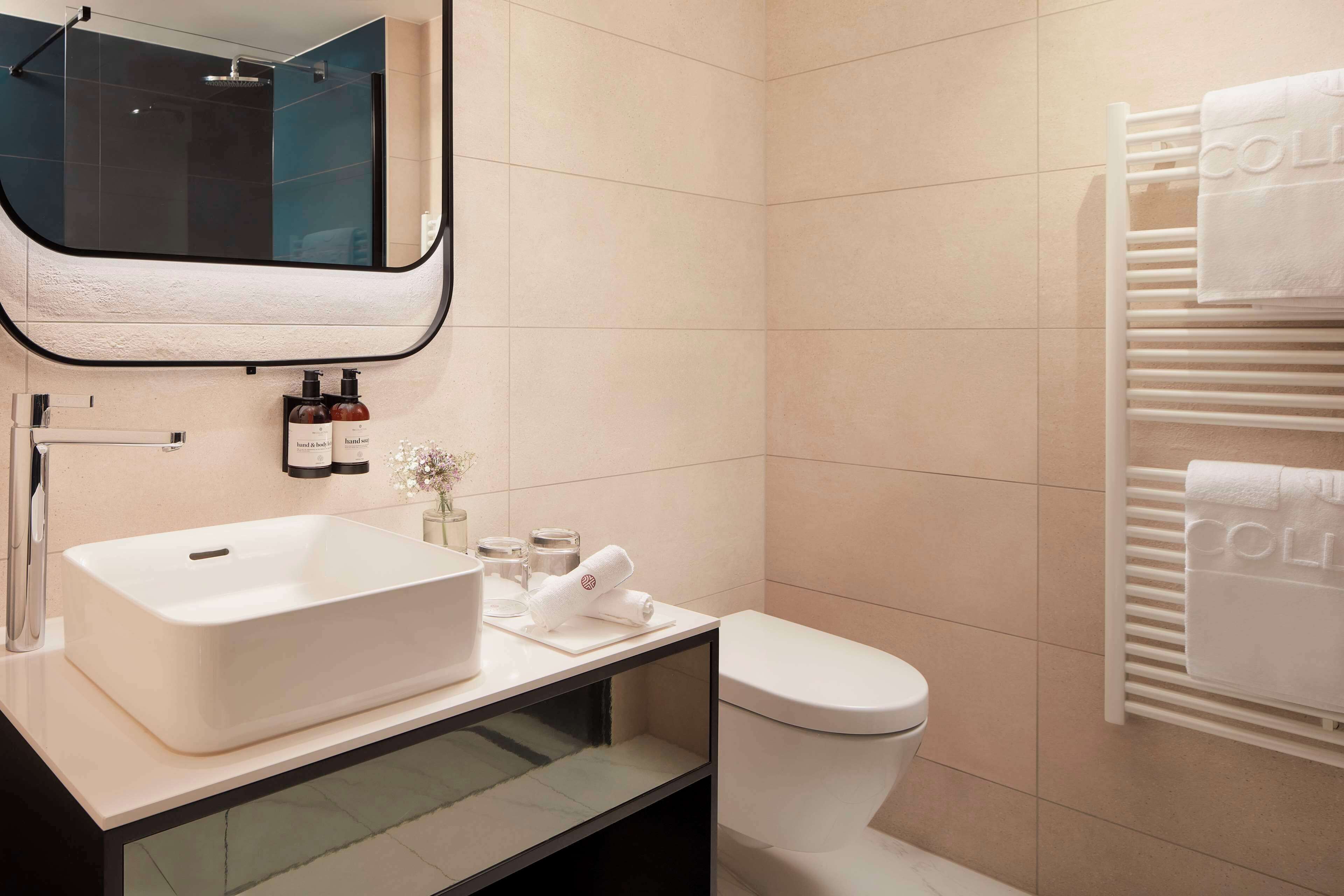 A modern bathroom with a large white sink, a toilet, and a towel rack with towels.