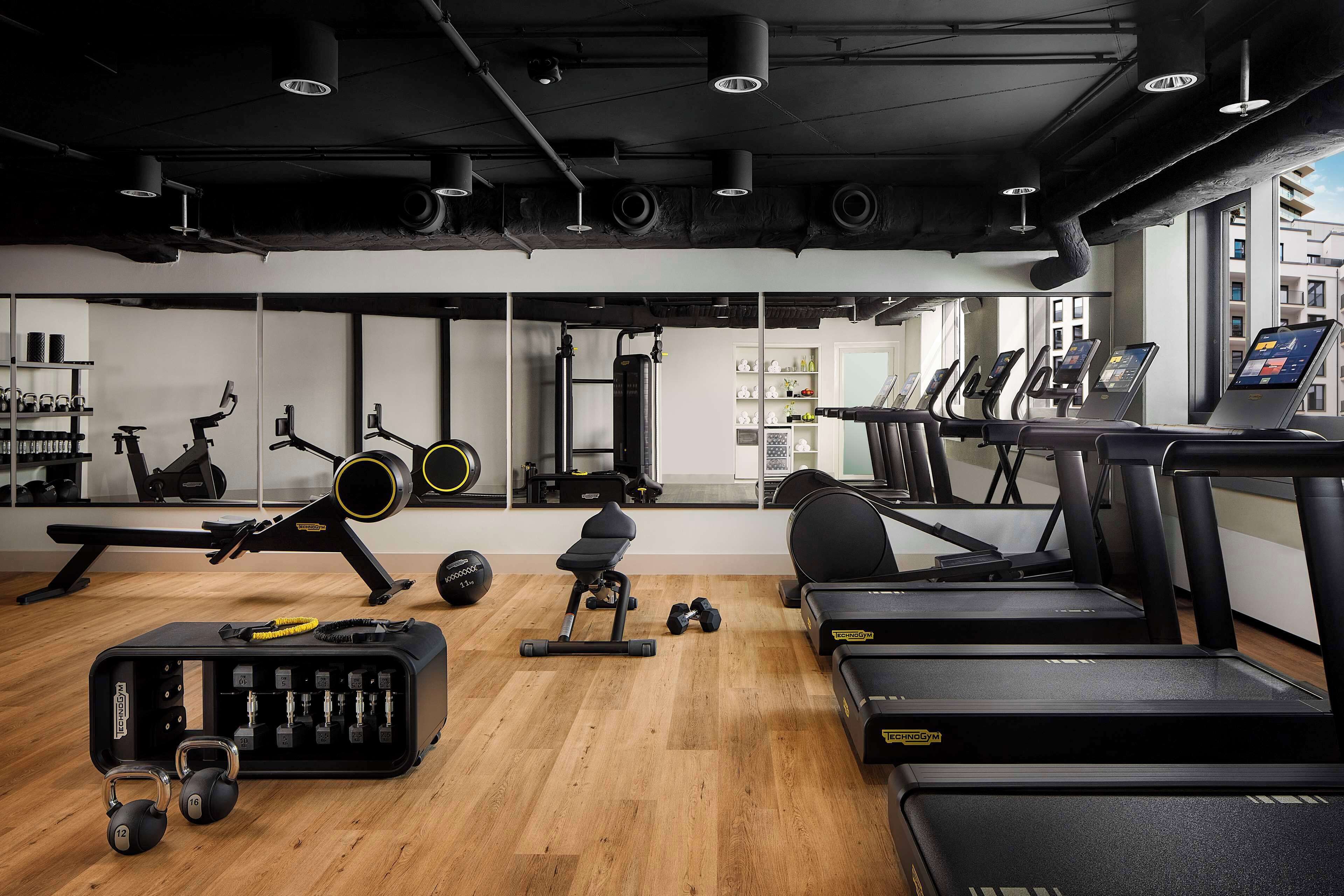 Ein Fitnessraum mit Laufbändern, Rudergerät, Kurzhanteln und einer Bank.