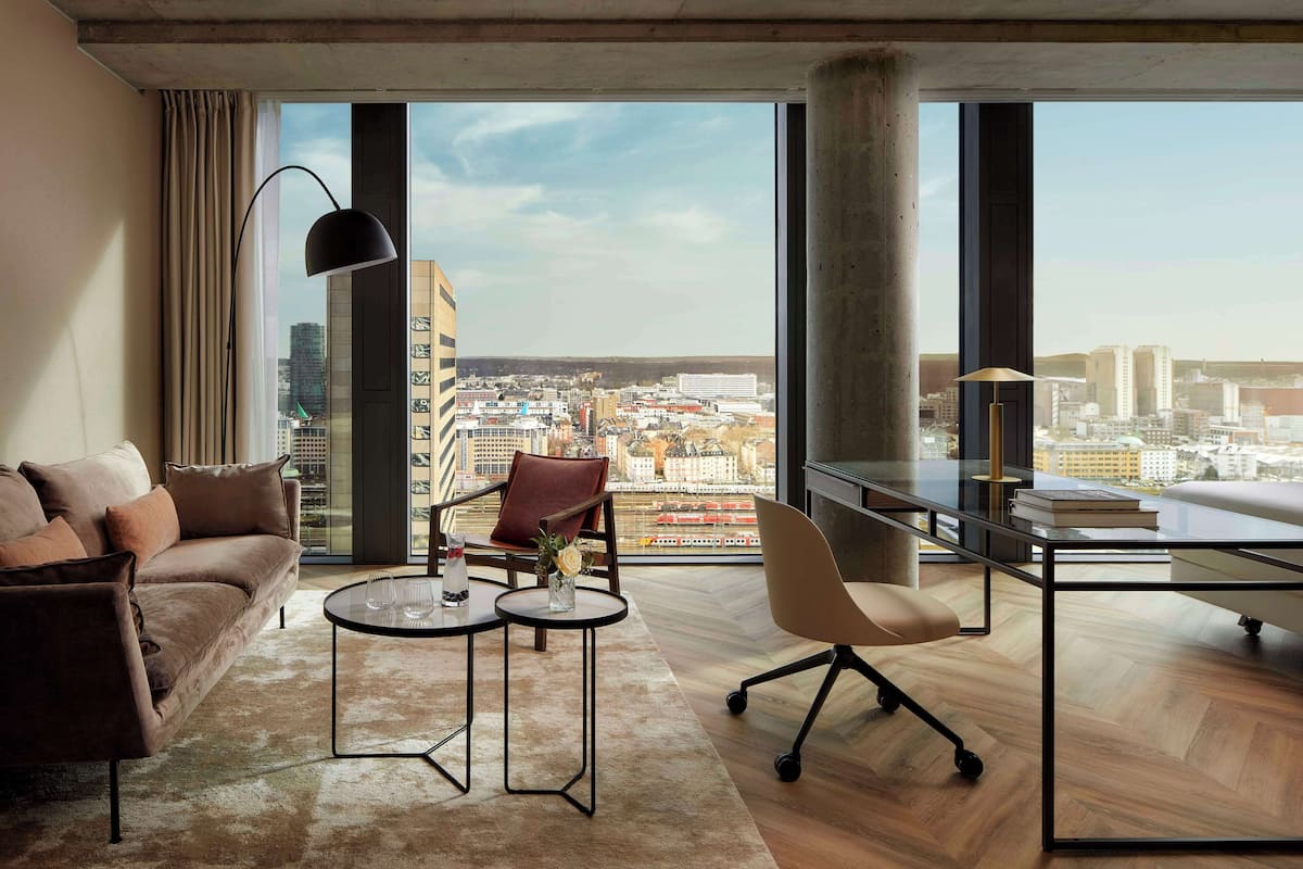 Een moderne woonkamer met een groot raam, een bank, een salontafel, een bureau en een stoel.