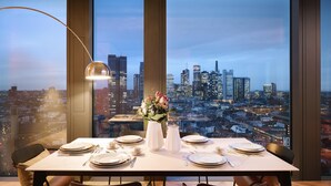 A dining table set for four with a cityscape view through large windows.