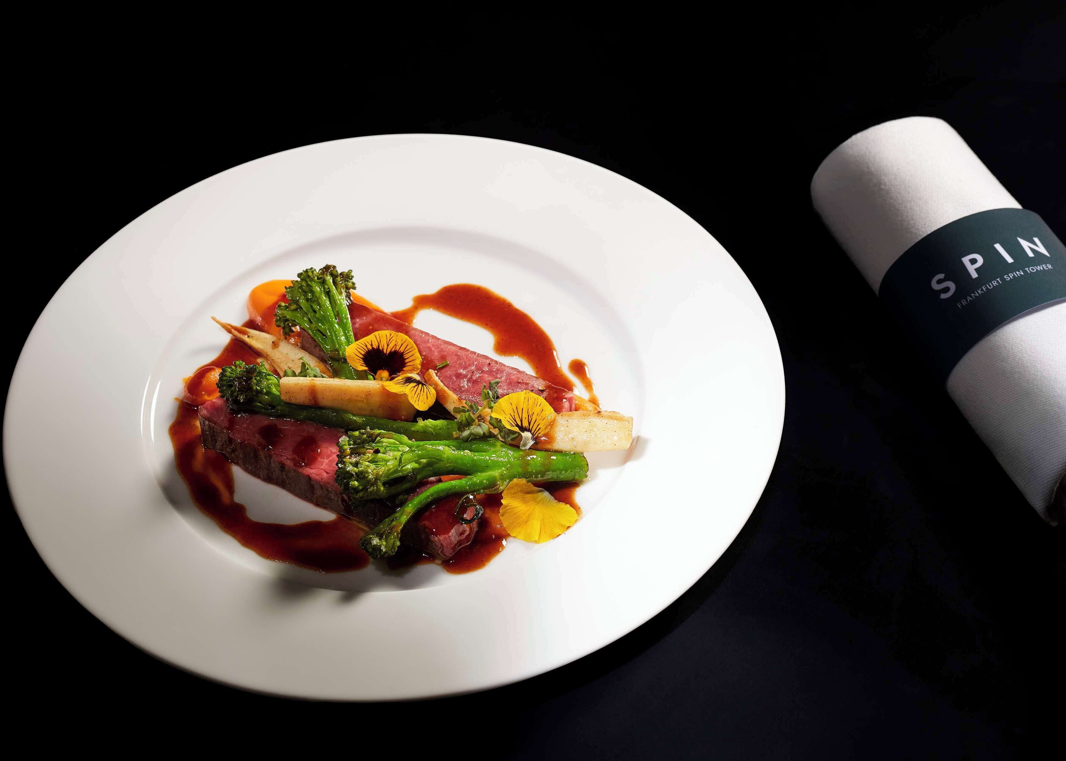 A white plate with a dish of steak, broccoli, and yellow flowers, accompanied by a bottle of wine.