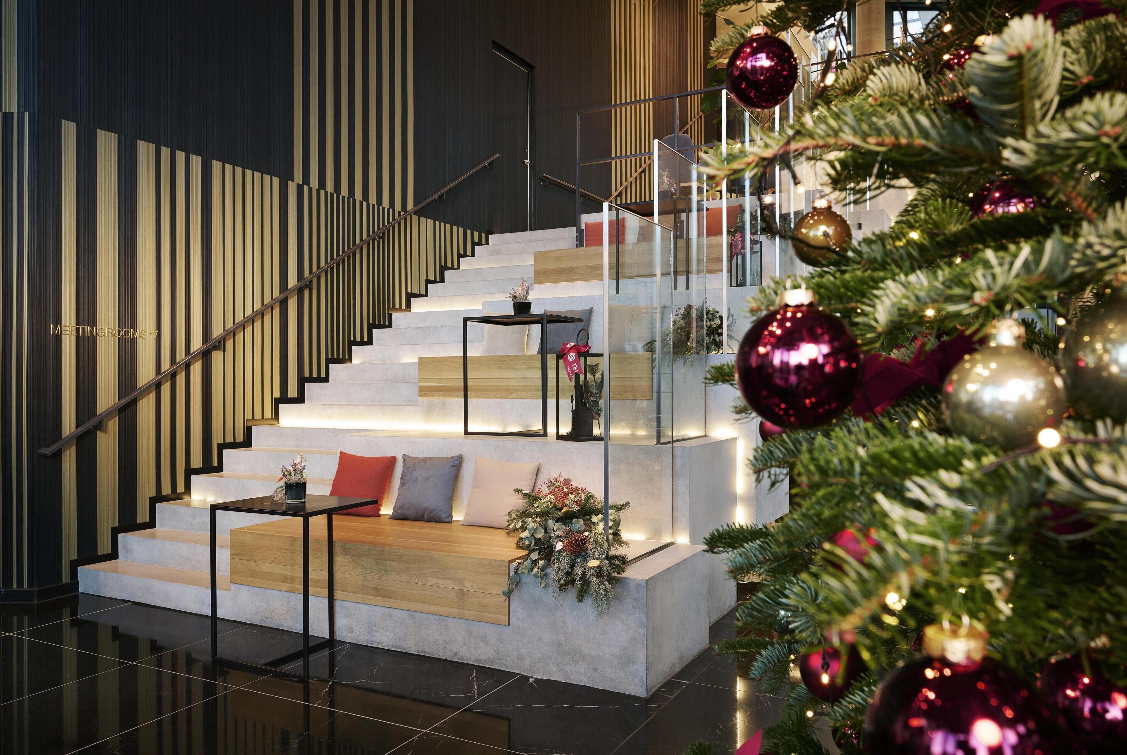 A modern staircase with a wooden bench and a small table, decorated with Christmas ornaments and a potted plant.