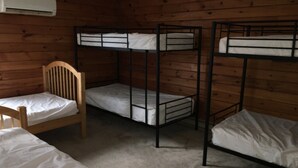 A bunk bed room with wooden walls, a single chair, and a ceiling-mounted air conditioner.