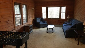 A cozy room with wooden walls, a foosball table, two sofas, and large windows.
