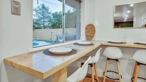 A modern kitchen with a large window, wooden countertop, white chairs, and a round woven table runner.