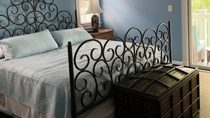 Ein Schlafzimmer mit einem Bett, einem Nachttisch, einer Lampe, einem Deckenventilator und einem Fenster mit Jalousien.