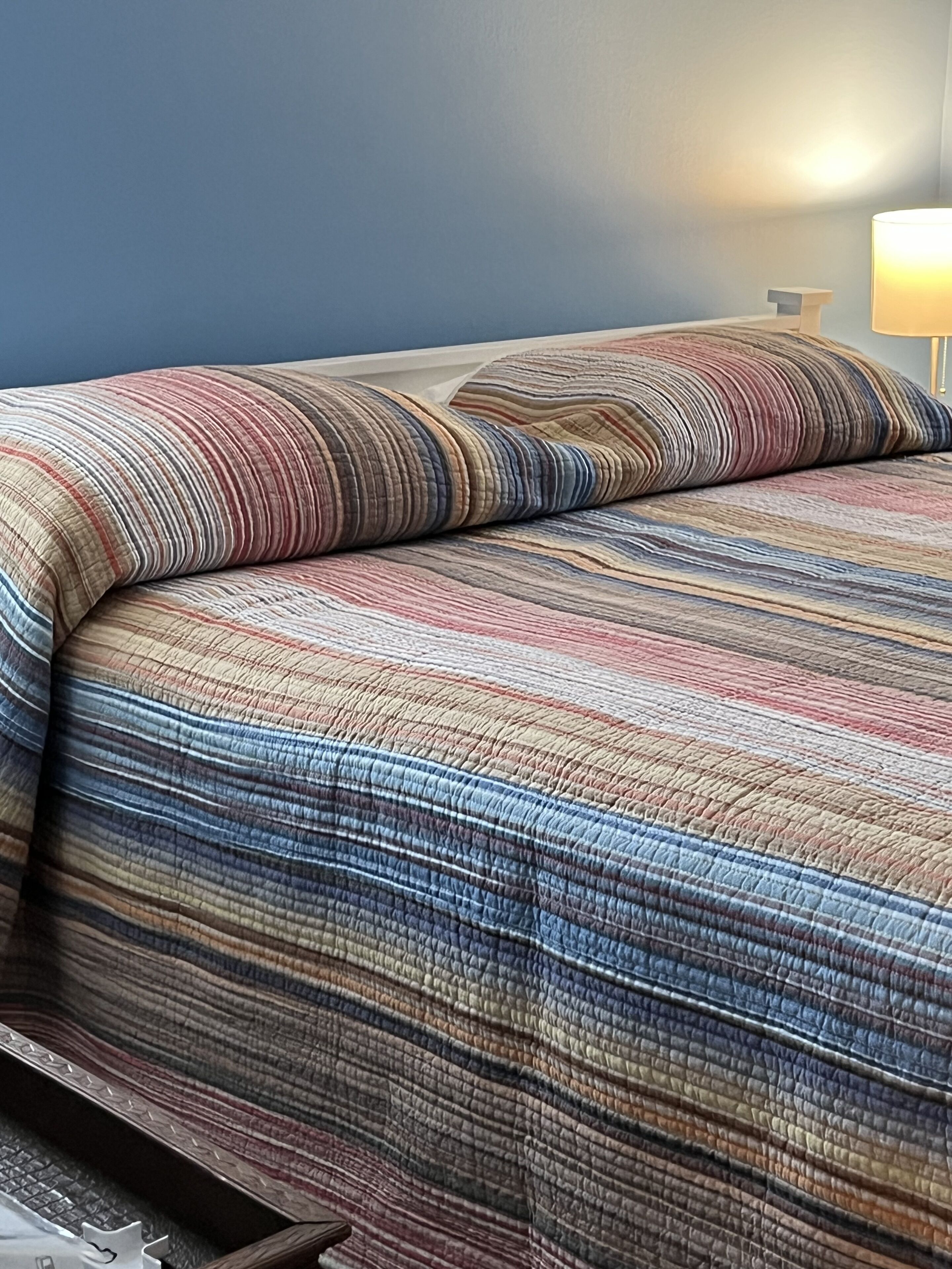 Un lit avec une couvre-lit à rayures et un seul oreiller.