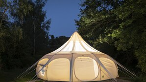 A dome-shaped tent with a central entrance, surrounded by a gravel area, set in a forested environment. - Orion 4-person Stunning Lotus Belle Tent (Ross-on-Wye)