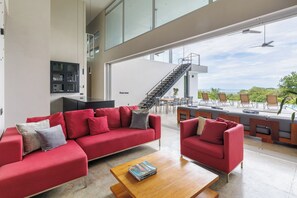 Ein modernes Interieur mit roten Sofas, einem Holztisch und Blick auf Sitzgelegenheiten im Freien sowie eine Treppe.