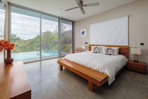 Ein Schlafzimmer mit einem großen Bett, einer Bank, einem Deckenventilator, Blick auf einen Swimmingpool und einem großen Fenster.