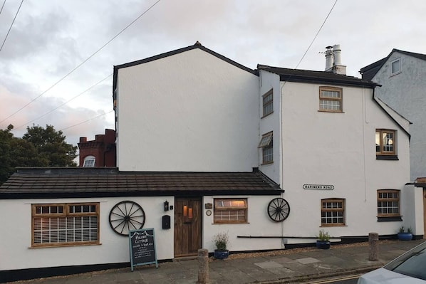 Un edificio blanco con un letrero que dice "Mariners Road" y un cartel anunciando "Holiday Cottage" disponible para reservar.