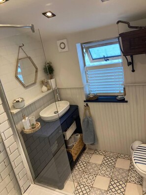 Un baño con cabina de ducha de vidrio, lavamanos, inodoro y ventana con persianas.