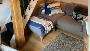 Ett mysigt vardagsrum med en trätrappa, en soffa med mönstrade kuddar och en inramad tavla på väggen.