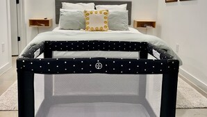Een slaapkamer met een bed, een raam, een ledikant en kunstwerken aan de muur.
