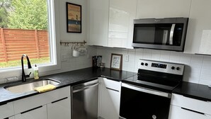 Een moderne keuken met witte kasten, een RVS vaatwasser, een magnetron en een fornuis.