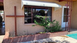 A building with a red brick facade, a white awning over a window, and a small garden area with a brick planter and green plants.