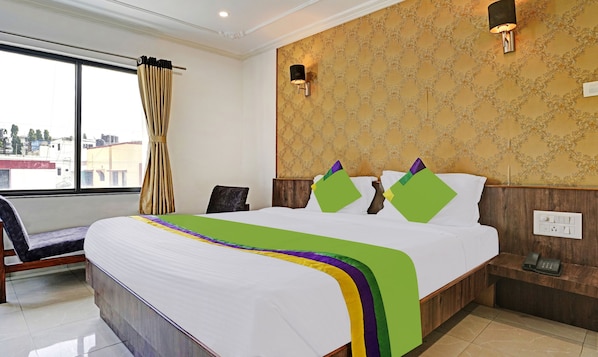 A hotel room with a large bed, a wooden headboard, a nightstand with a phone, and a window with curtains.