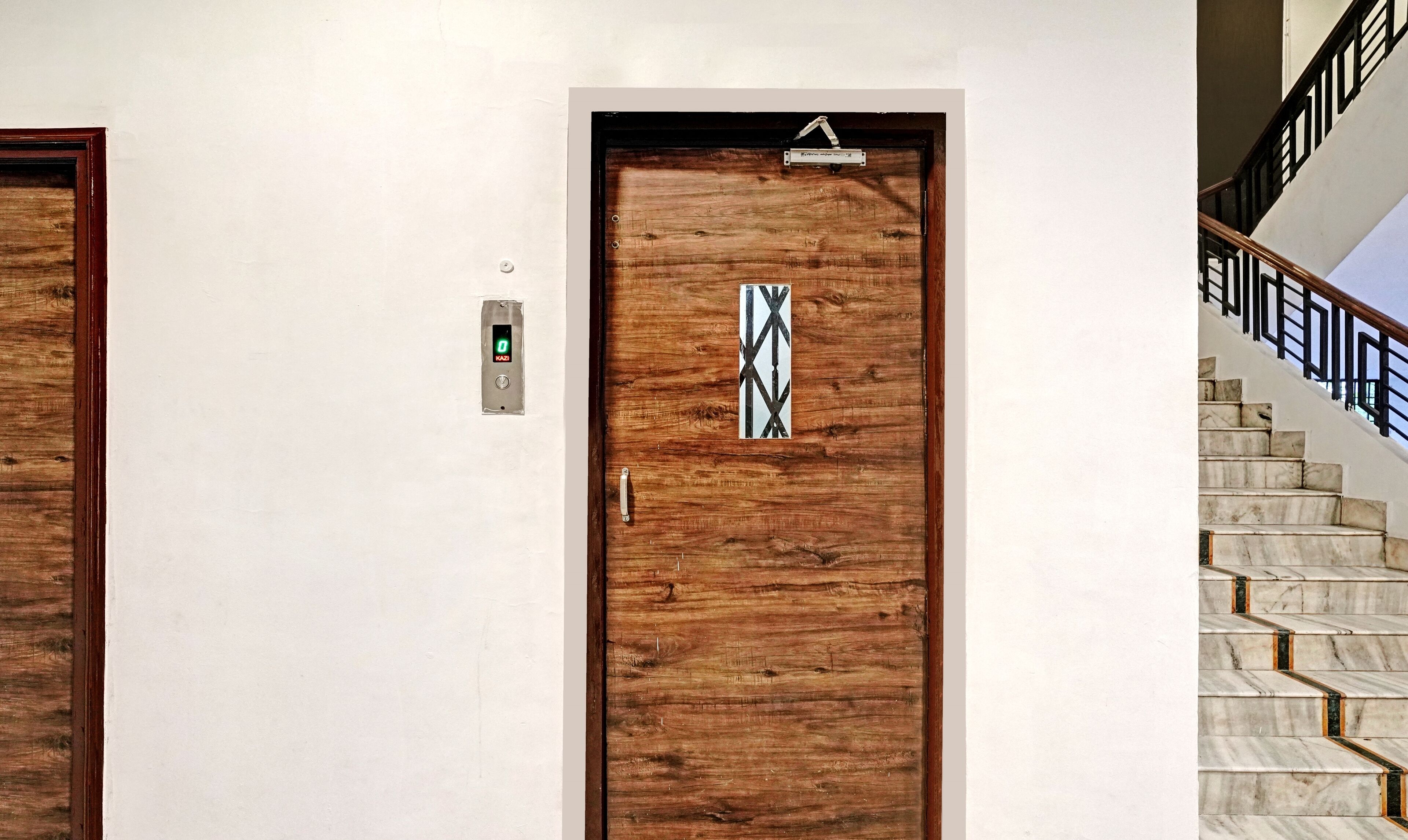 A wooden door with a digital lock and a keypad, a marble staircase with black railings, and a white wall.