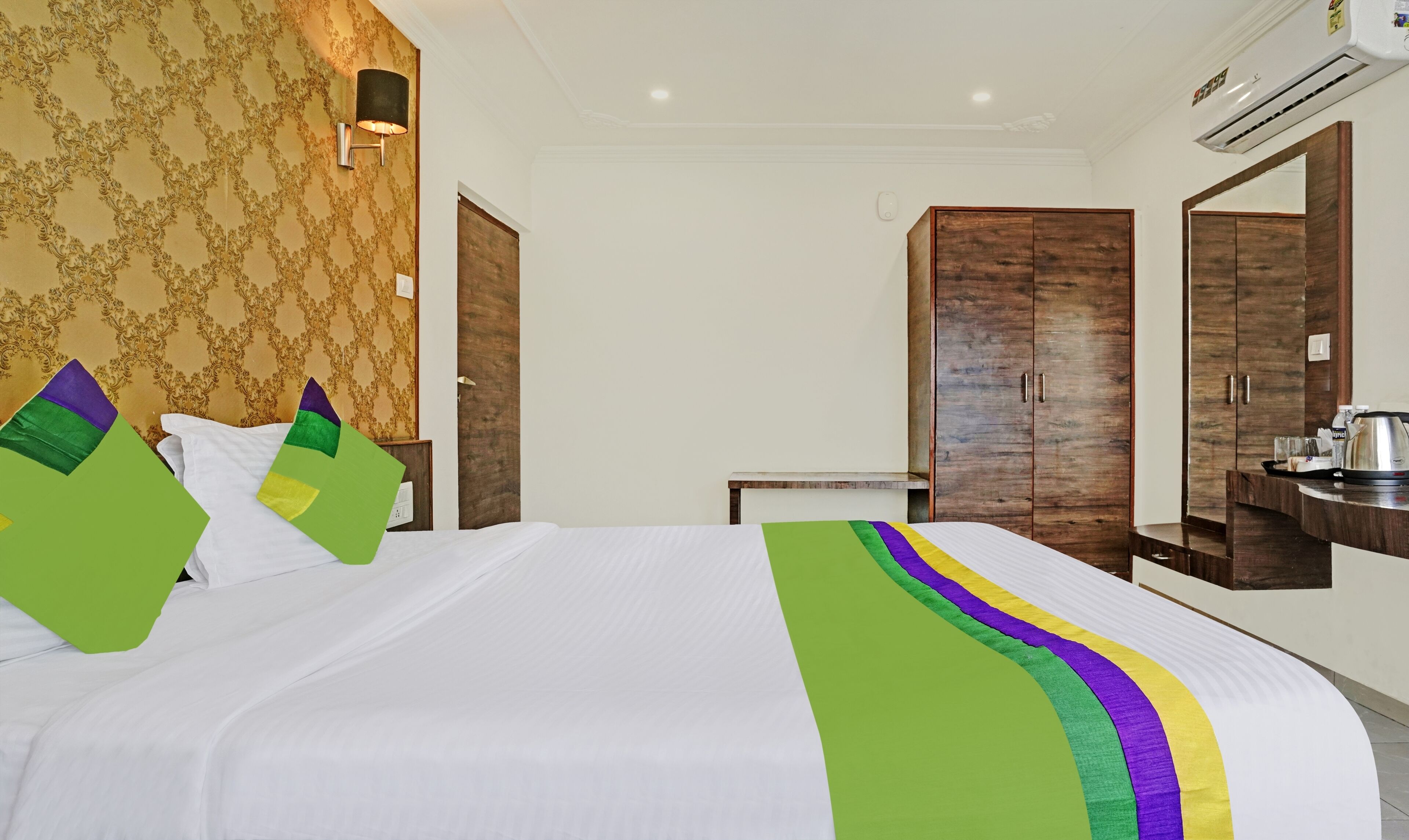 A hotel room with a neatly made bed, a wooden wardrobe, a small table, and an air conditioning unit.