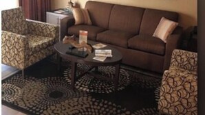 Una sala de estar con un sofá marrón, sillones estampados, una mesa de centro y un cuadro en la pared.