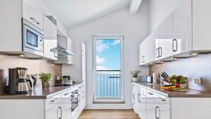 Una cocina moderna con armarios blancos, piso de madera y vista al cielo a través de un ventanal amplio.