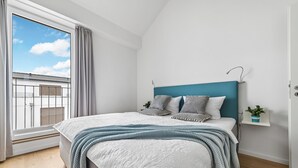 Un dormitorio con una cama, vistas del cielo, una ventana y una pequeña planta en un estante.