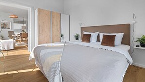 A modern bedroom with a large bed, wooden wardrobe, and a small bedside table.