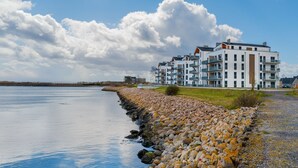 A waterfront property with a rocky shoreline, modern buildings, and a clear sky.