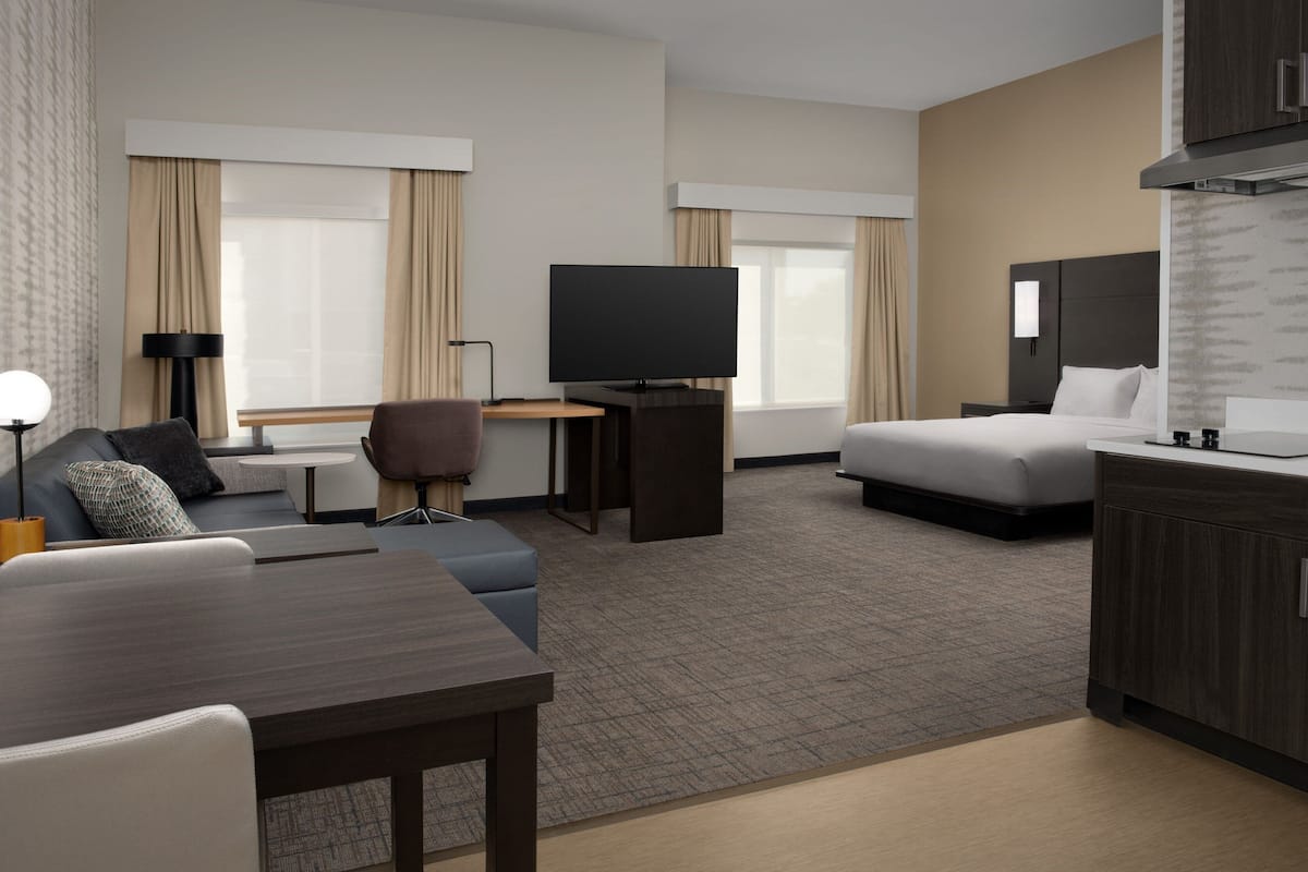 A hotel room with a sofa, a desk with a television, a bed, and a kitchenette.