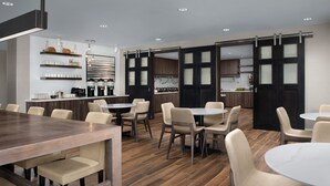 A modern dining area with wooden tables and chairs, a kitchen in the background, and a sliding door with frosted glass panels. - Residence Inn By Marriott Fresno Clovis (Clovis)