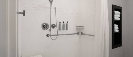 Un baño moderno con cabina de ducha, barras de apoyo, toallero y inodoro con asiento de seguridad.