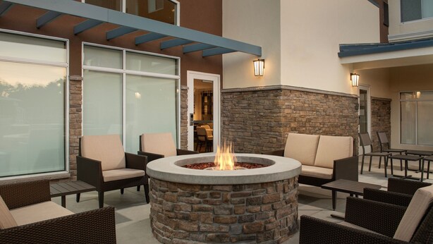A circular stone fire pit surrounded by wicker furniture in an outdoor patio area. - Residence Inn By Marriott Fresno Clovis (Clovis)