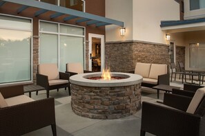 A circular stone fire pit surrounded by wicker furniture in an outdoor patio area. - Residence Inn By Marriott Fresno Clovis (Clovis)