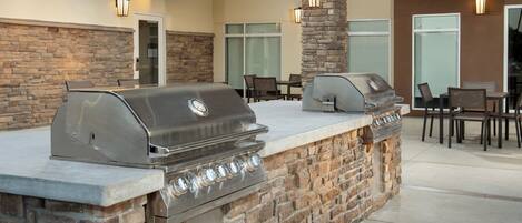 An outdoor kitchen with two grills, stone walls, and outdoor seating.