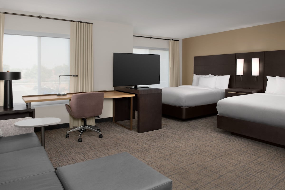 A hotel room with a bed, a desk with a TV, a chair, and a sofa.