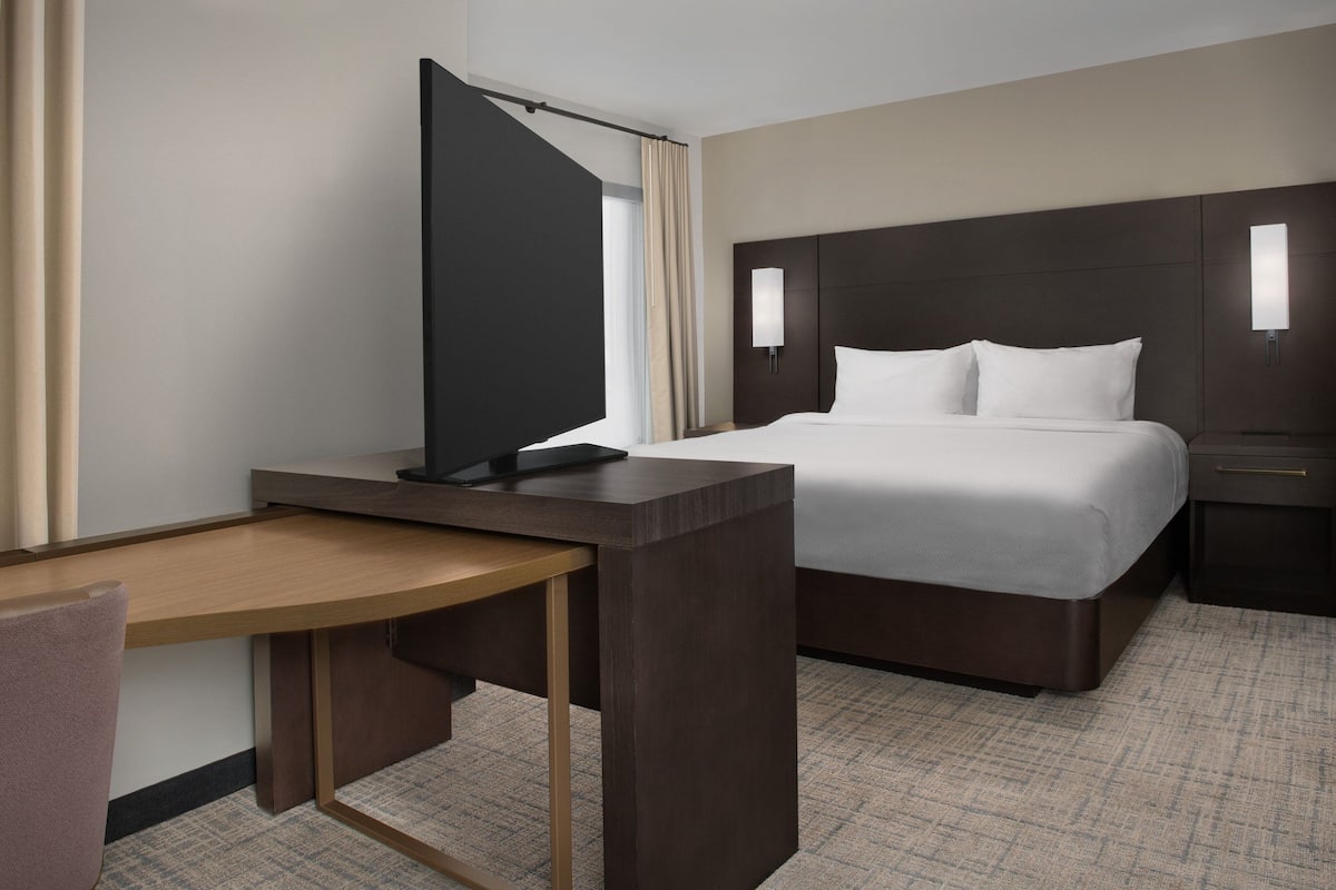 A hotel room with a bed, a desk, a chair, a TV, and a nightstand.