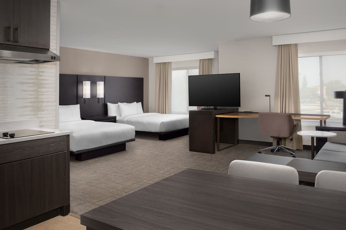 A modern hotel room with a large bed, a desk, a TV, and a seating area.