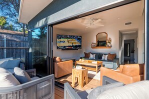 Ein modernes Wohnzimmer mit Glastür, Deckenventilator, Flachbildfernseher und einer gemütlichen Sitzecke mit Couchtisch.