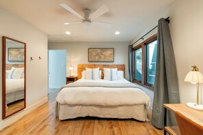 Une chambre à coucher avec un lit, un ventilateur de plafond, une table de chevet, une lampe, une fenêtre avec des rideaux et une carte accrochée au mur.