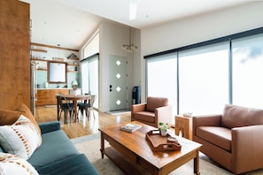 Una sala de estar moderna con sofá, sillones, una mesita de centro y un comedor, con una cocina al fondo.