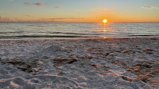 Une plage avec un coucher de soleil sur l’océan.