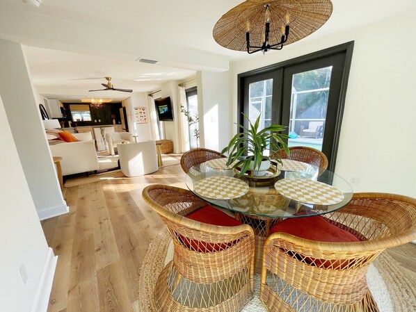 A dining area with wicker chairs, a glass table, and a ceiling fan.