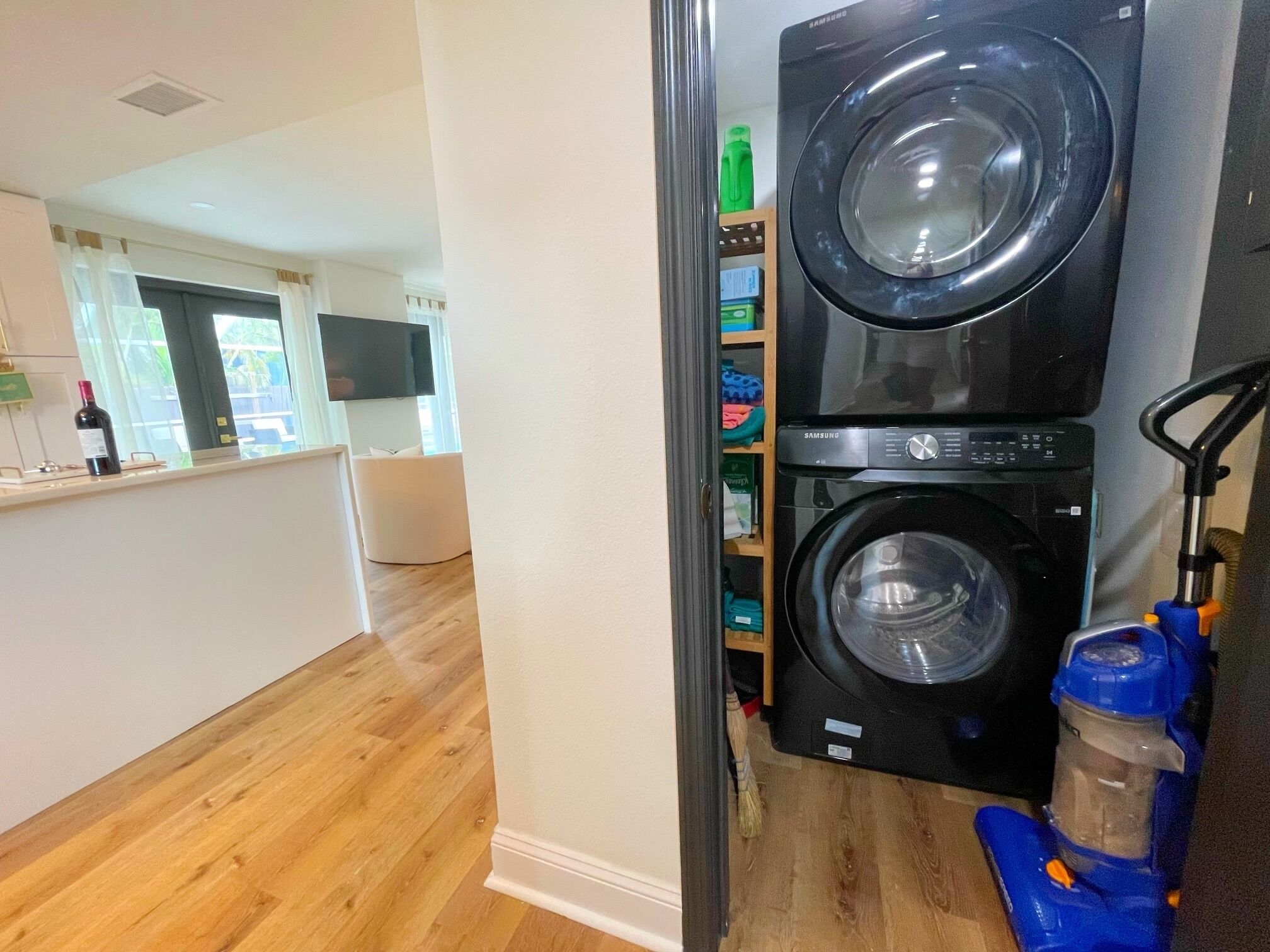 Une buanderie équipée de deux machines à laver Samsung noires, d’un aspirateur bleu et d’un plancher en bois.