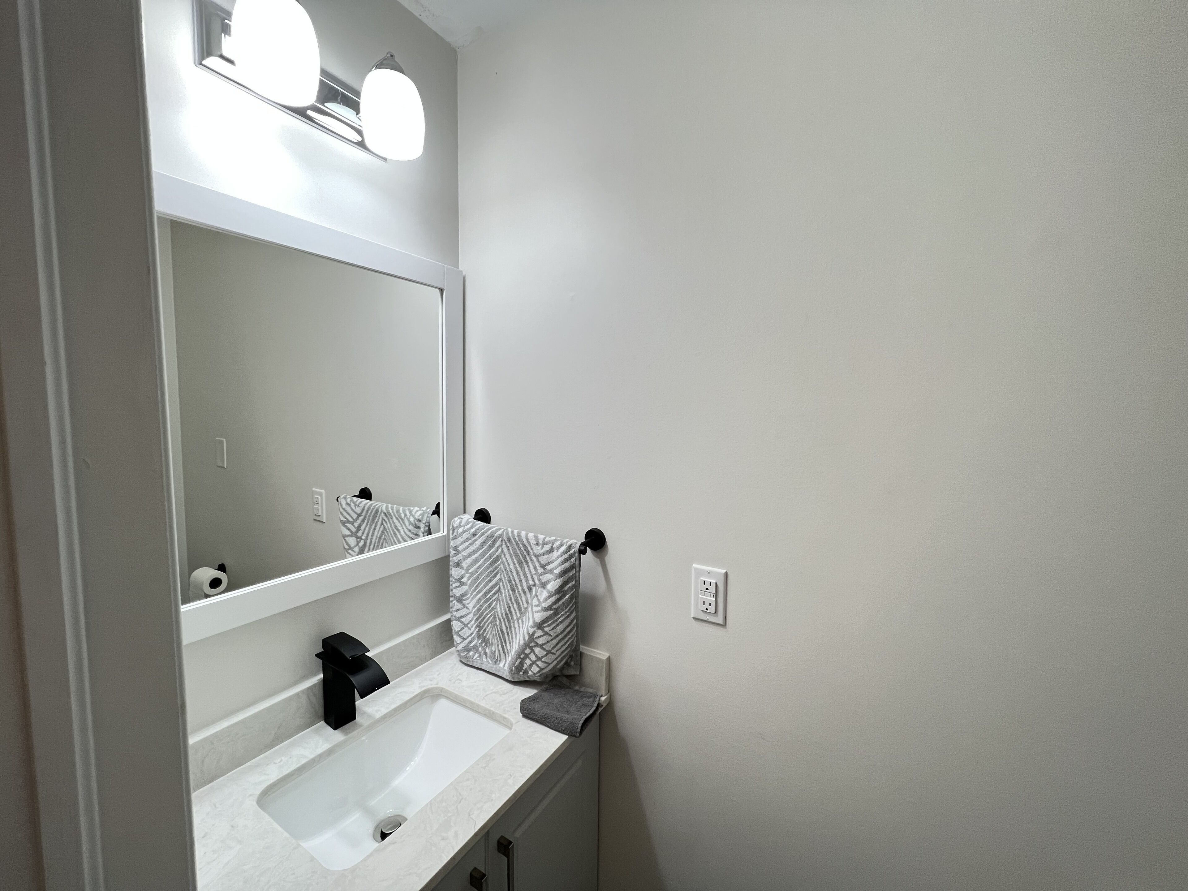 Un baño con un lavabo blanco, un espejo y un perchero para toallas.