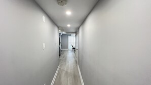A narrow hallway with grey walls and a wooden floor, leading to a door at the end.