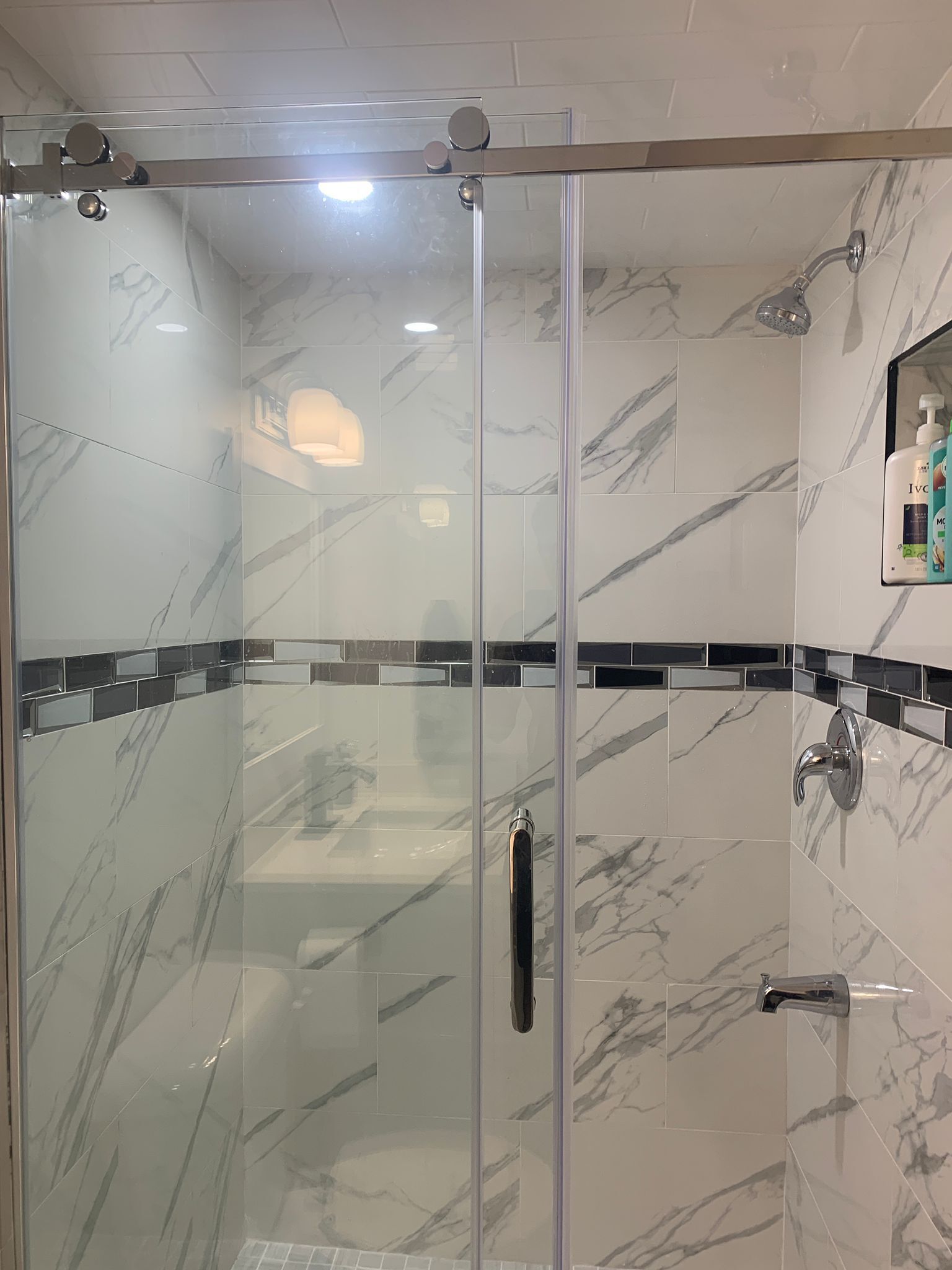 A glass-enclosed shower area with marble tiles and a handheld showerhead.